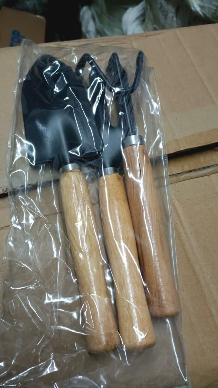Set of gardening tools with wooden handles in clear plastic packaging on a cardboard surface.