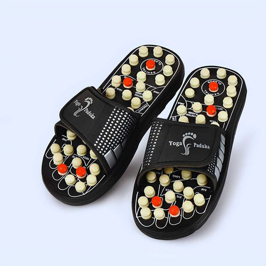 Pair of black yoga paduka shoes with acupressure nodes on a light gray background