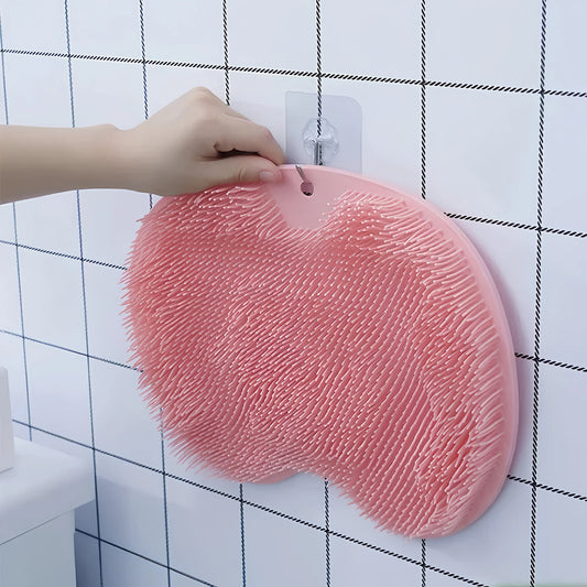 Silicone foot scrubber mat hanging on bathroom wall hook showing soft bristle side in pink